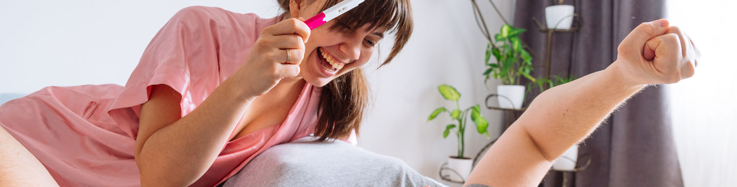 happy couple in bed. woman showing man positive pregnancy test.