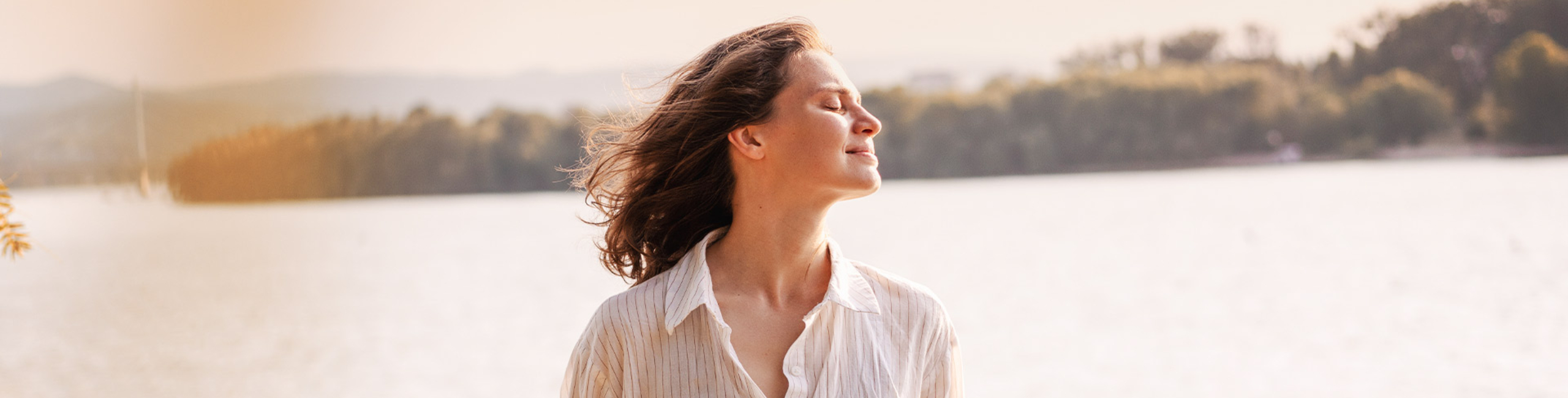 Žena stoji vani uz jezero i uživa u suncu zatvorenih očiju