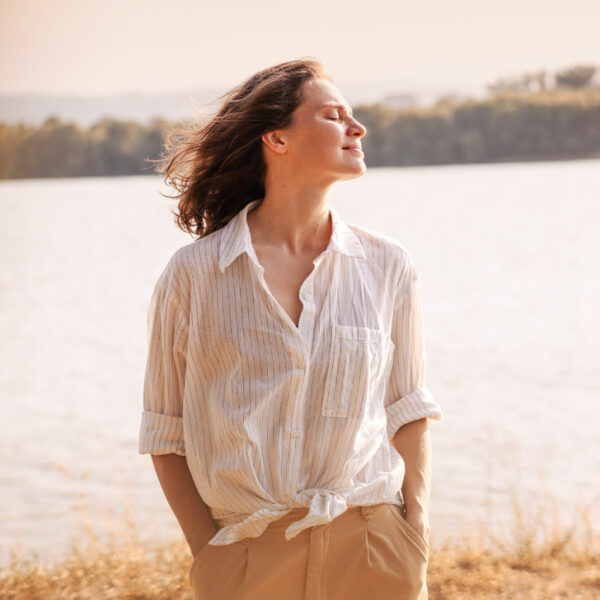 Žena stoji vani uz jezero i uživa u suncu zatvorenih očiju